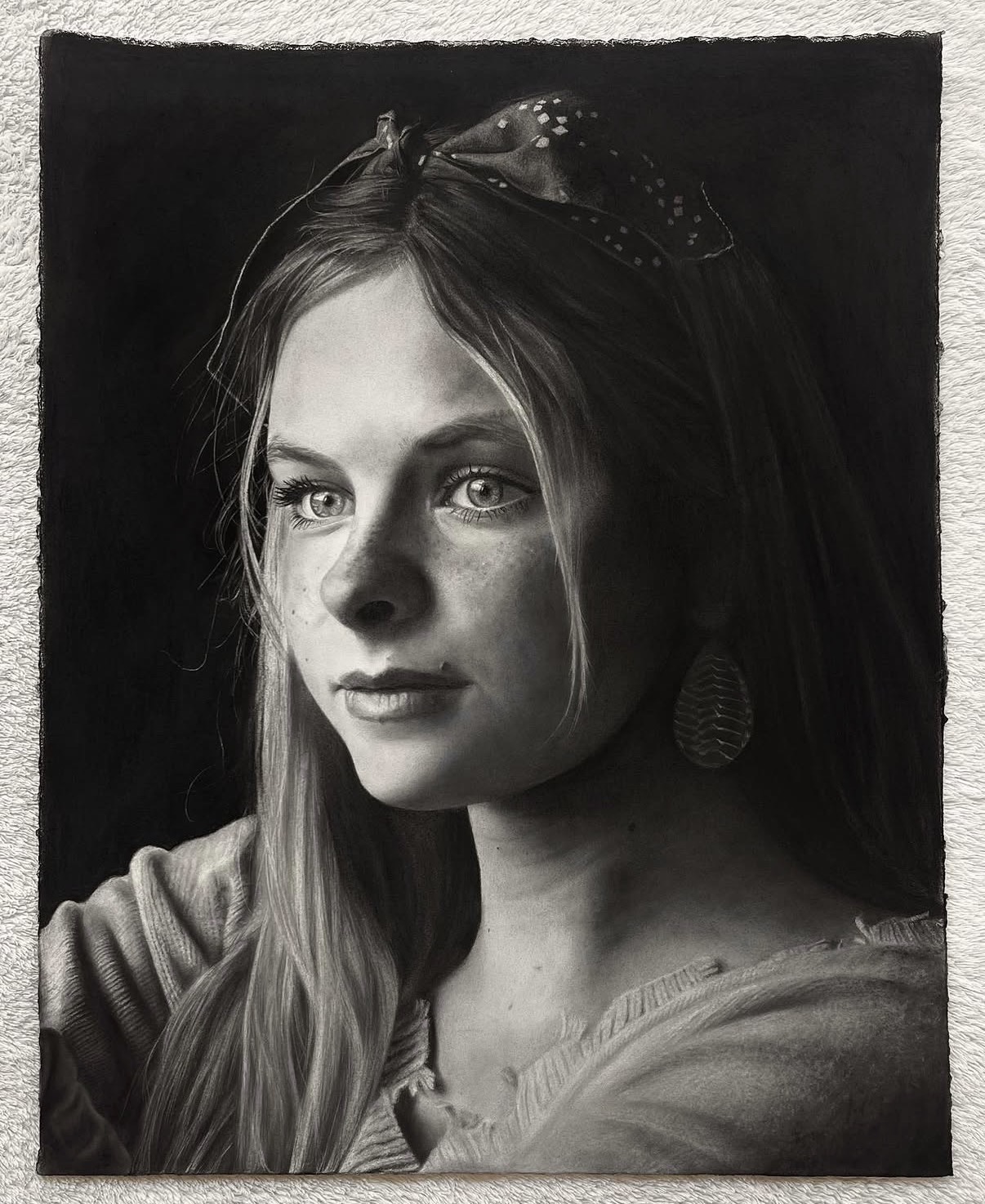 A graphite portrait of a young woman, hung in a plain wood moulding.